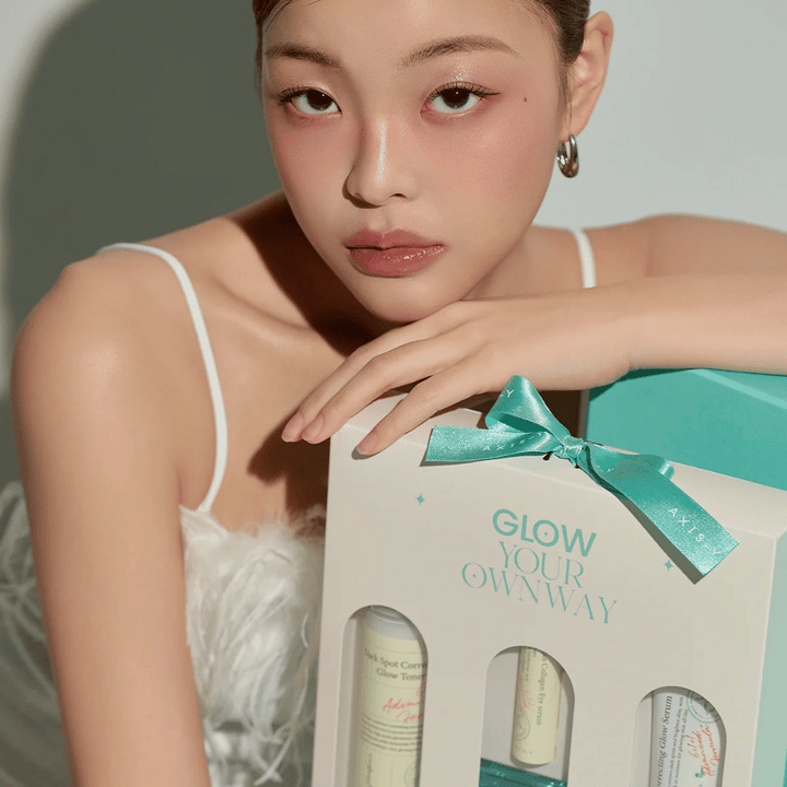 Modell med elegant makeup håller i AXIS-Y:s “Glow Your Own Way”-gåvobox – ett stilrent hudvårdskit perfekt som present till dig själv eller någon du tycker om.