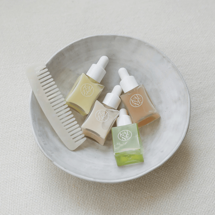 Fyra små serumflaskor från KAINÉ Serum Discovery Kit ligger i en vit skål bredvid en kam, med en naturlig och lugn bakgrund i beige ton.
