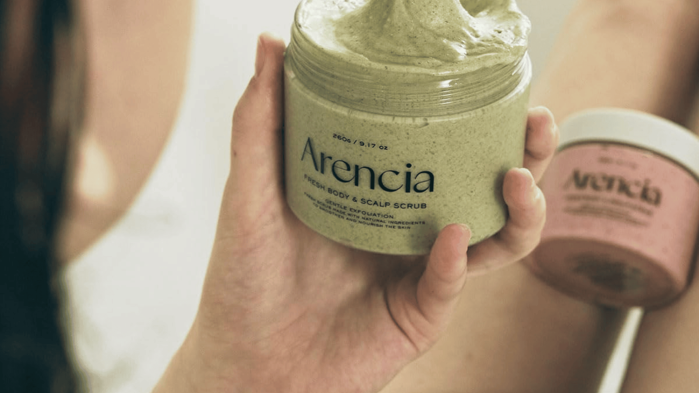 Arencia Fresh Body & Scalp Scrub hålls i handen. Naturlig kroppsskrubb och skalpskrubb som exfolierar skonsamt, rengör huden på djupet och lämnar en mjuk, fräsch känsla.