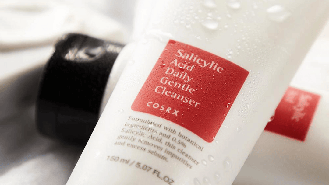 Närbild på en flaska av COSRX Salicylic Acid Daily Gentle Cleanser med vattendroppar, på en suddig bakgrund.