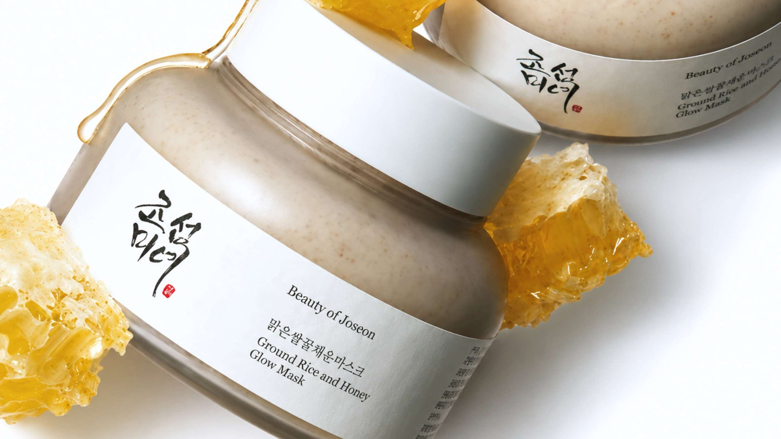 En öppen burk med Skinfood Black Sugar Perfect Essential Scrub 2X, bredvid dess svarta lock, på en brun bakgrund.