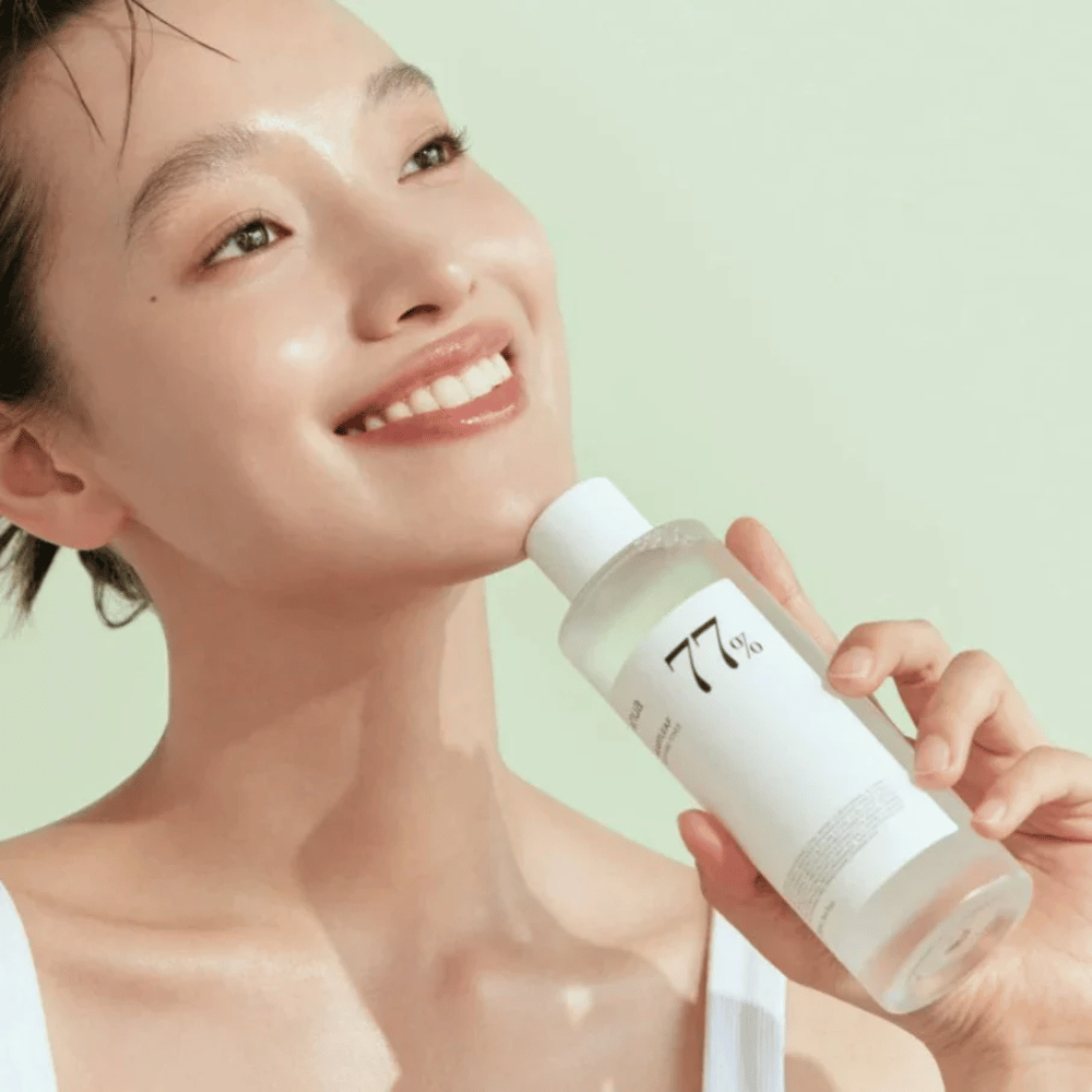A woman soothes her sensitive skin with a bottle Heartleaf 77% Soothing Toner from Anua, containing chameleon leaf extract.