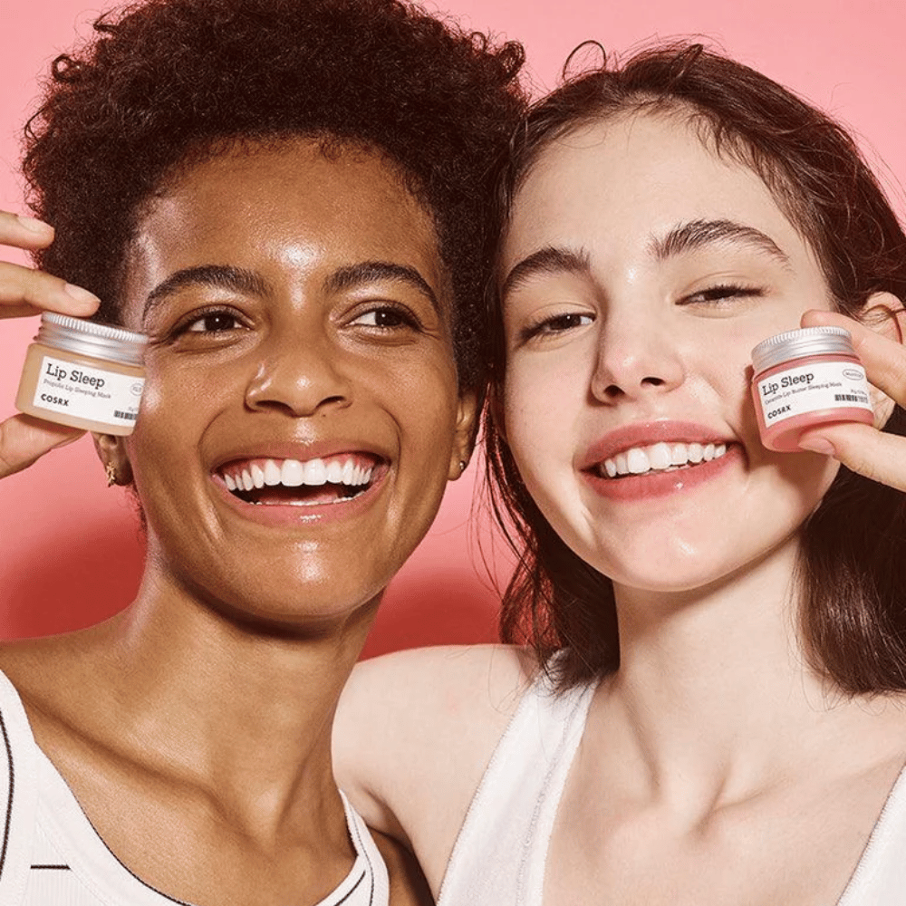 Two people smile and hold up COSRX Lip Sleep jars. The image conveys soft, hydrated lips and the product's natural glow-giving effect.
