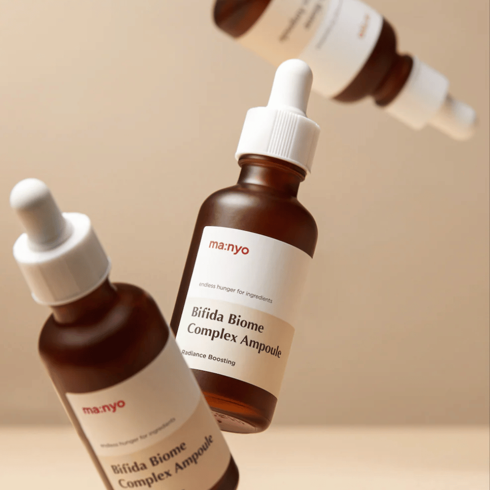 Product image with several floating bottles of ma:nyo Bifida Biome Complex Ampoule against a beige background, creating a modern and minimalist feel.