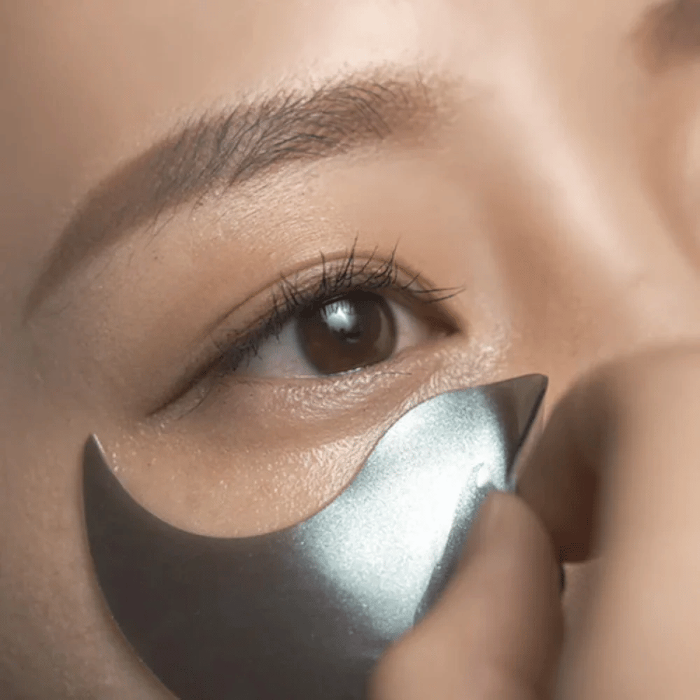 Detailed image showing a black hydrogel eye patch being applied under the eye. The image shows the snug fit and the cooling sensation around the eye area.