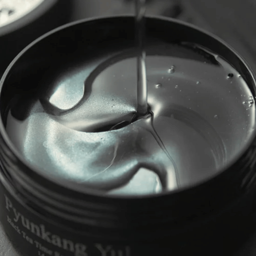 Close-up of black hydrogel eye patches in an open jar from Pyunkang Yul. The glossy patches rest in serum and highlight the product’s moisturizing and luxurious feel.