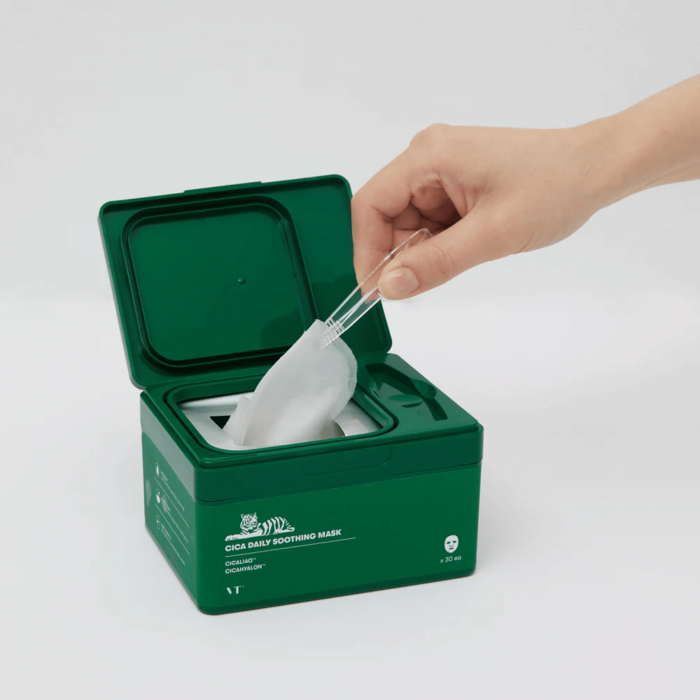 Hand uses tweezers to pick up a Sheet mask from a green container labeled "Cica Daily Soothing Mask".
