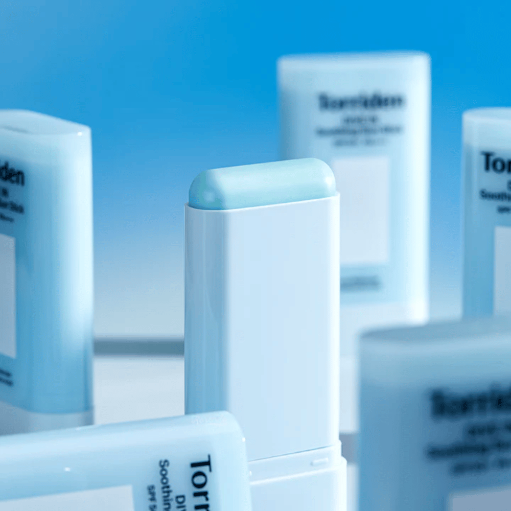 Close-up of Torriden DIVE IN Soothing Sun Stick showing the soft sunscreen formula in stick format with multiple products in the background.