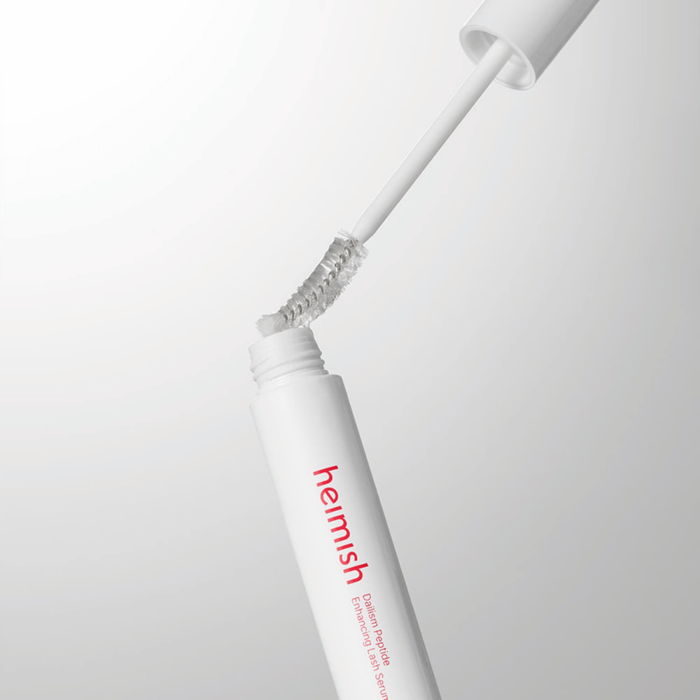 Close-up of the applicator for Heimish Dailism Peptide Enhancing Lash Serum. The brush is pulled up from the white container and shows the transparent serum formula that is applied to the lashes.