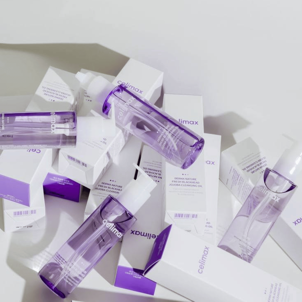 Celimax Derma Nature Fresh Blackhead Jojoba Cleansing Oil in purple bottles placed among white product packages with purple details.