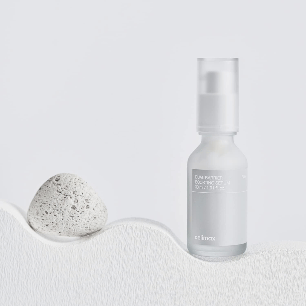 Celimax Dual Barrier Boosting Serum placed on textile with stone, calm product image signaling hydration and strengthened skin barrier.