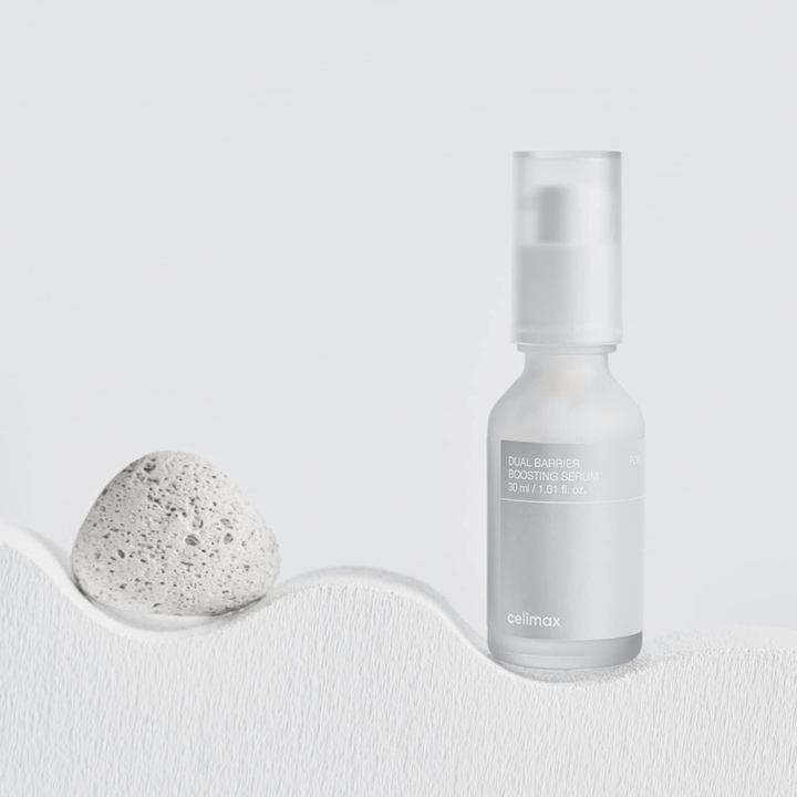 Celimax Dual Barrier Boosting Serum placed on textile with stone, calm product image signaling hydration and strengthened skin barrier.
