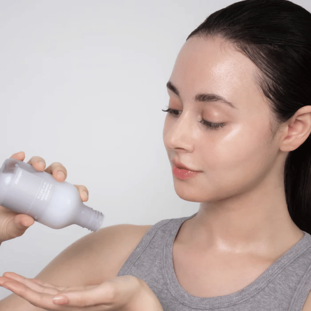 Woman with glossy, hydrated skin applies Celimax Dual Barrier Creamy Toner by pouring the product into her palm as part of her skincare routine.
