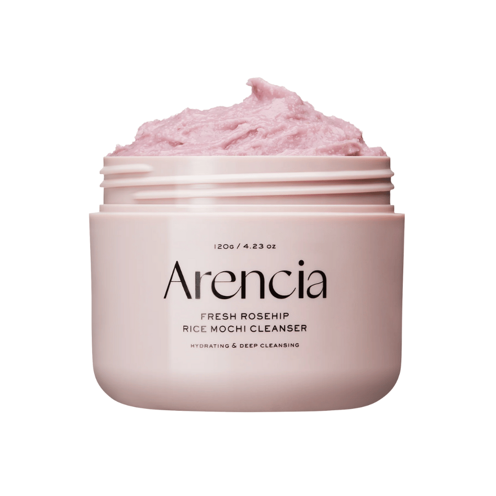 Close-up of a pink jar with Arencia Royal Rosehip Cleanser, filled with pink cleansing cream with a whipped, mochi-like texture. Text on the jar indicates that the product hydrates and deeply cleanses.