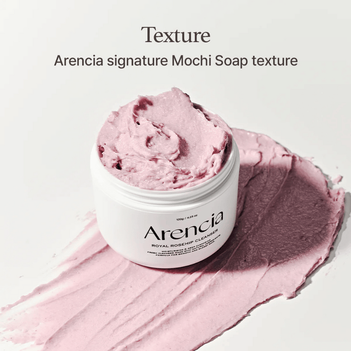 Burk med Arencia Royal Rosehip Cleanser syns ovanpå en utsmetad rosa rengöring med mochi-liknande textur. Texten ovanför beskriver produkten som Arencias signaturtextur.