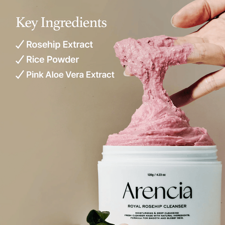 En hand lyfter upp den rosa, fluffiga rengöringstexturen från burken Arencia Royal Rosehip Cleanser, med ingredienslista till vänster: nyponextrakt, rispulver och rosa aloe vera-extrakt.