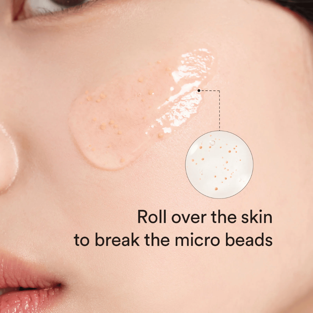 Close-up of a cheek with a serum containing small microbeads applied to the skin. A circular zoom shows the beads more clearly. The text says “Roll over the skin to break the micro beads.”