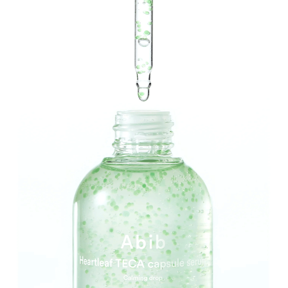 Minimalist close-up of serum bottle and dropper where the transparent formula with green capsules is the focus against a light background.