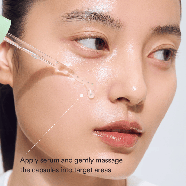 Close-up of model applying the serum with a dropper while the green capsules are massaged into the skin for a soothing and moisturizing effect.