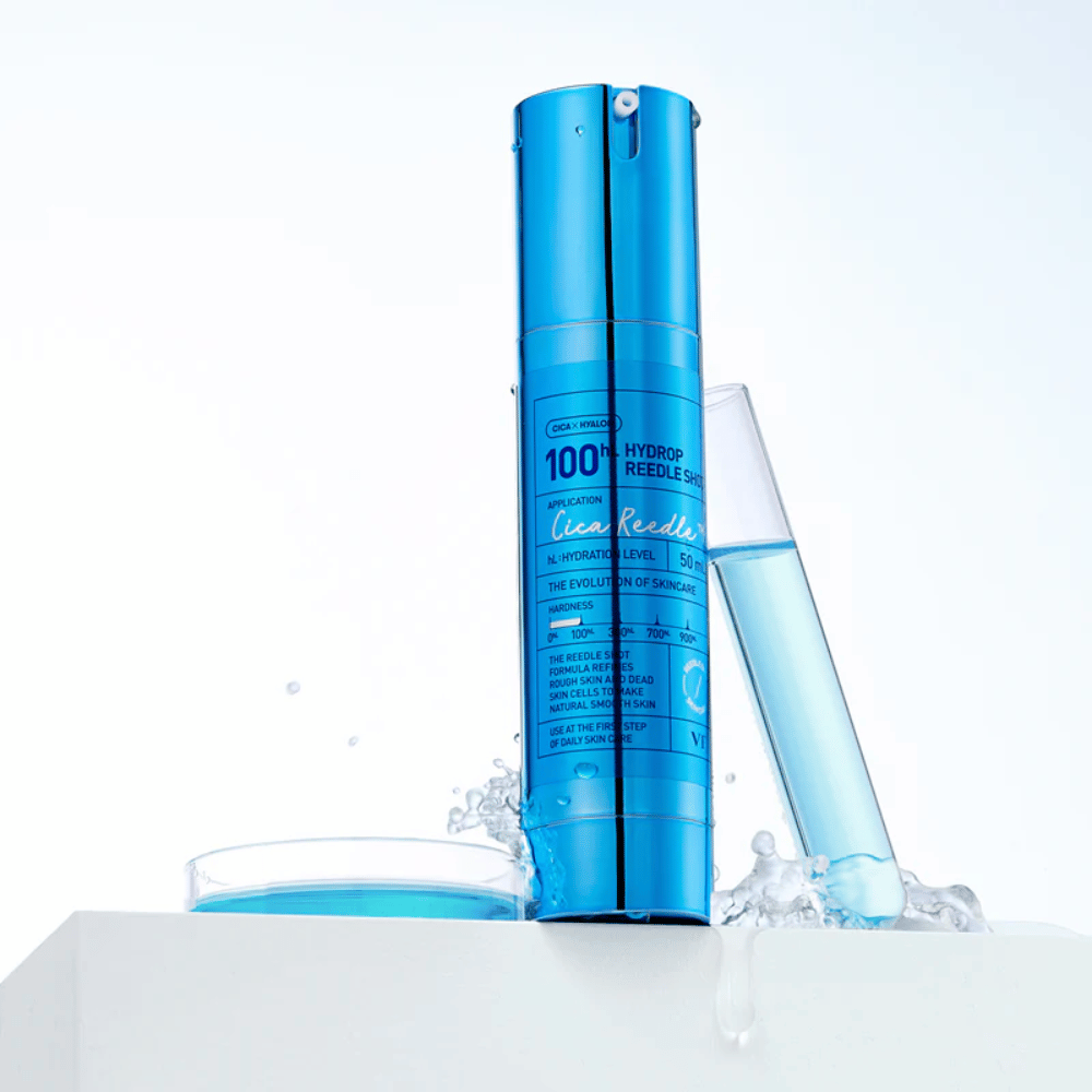 Blue bottle VT Cica Hyalon Hydrop Reedle Shot 100hL standing on a white surface with water splashes, next to a test tube filled with blue liquid and a round cap with the same liquid.