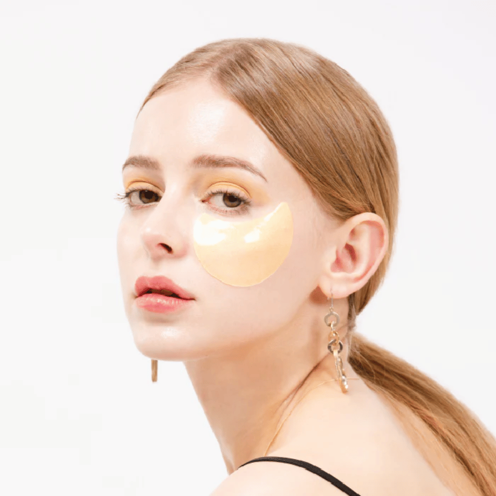 Modell bär ett guldskimrande hydrogel eye patch under ögat för lystergivande effekt.