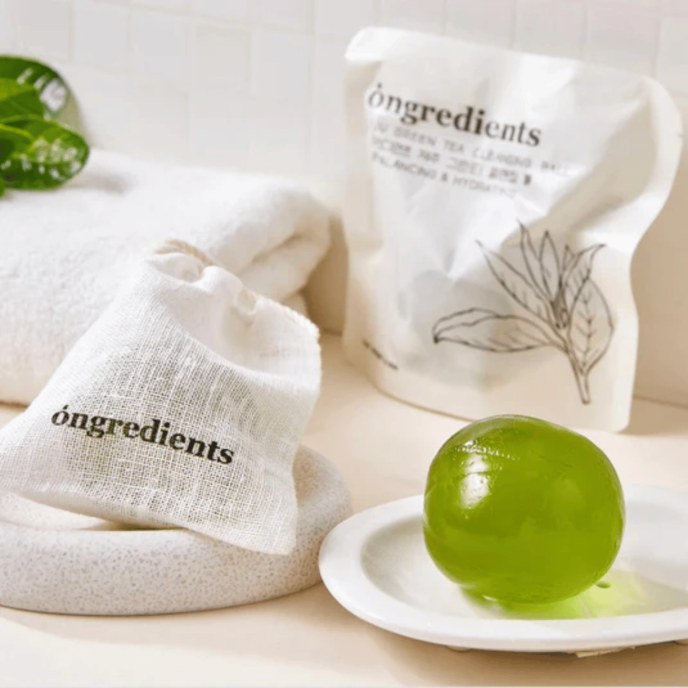 Óngredients Jeju Green Tea Cleansing Ball placed on a dish with packaging and towel – gentle cleanser with green tea from Jeju.