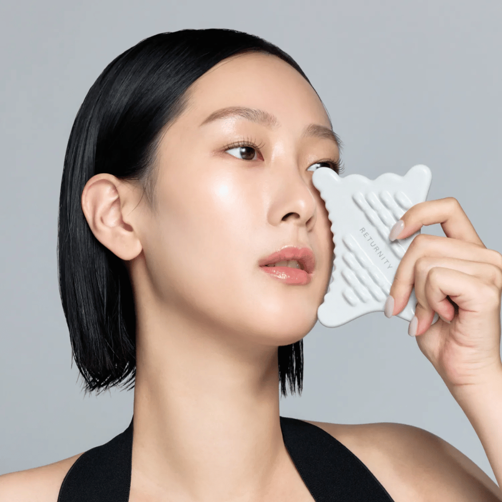 Close-up of model using RETURNITY Mini Guasha around the eye and cheek area for massage and relaxing skincare.
