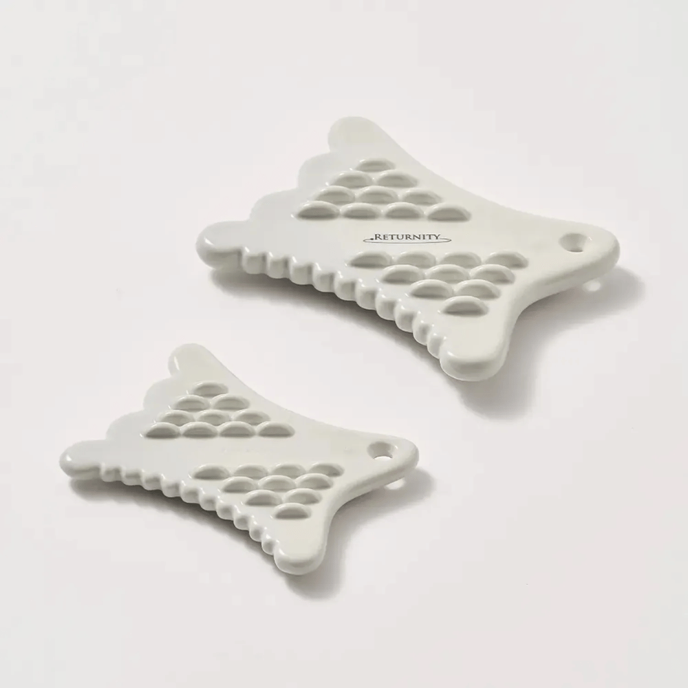 Two white RETURNITY Mini Guasha tools with a textured surface and ergonomic design on a light background.