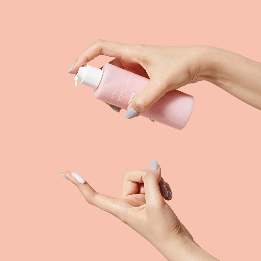 The image shows someone's hands holding a bottle with ANUA Peach 77% Niacin Conditioning Milk. This skincare product appears to have a milky consistency and is designed to care for and improve the skin's condition.