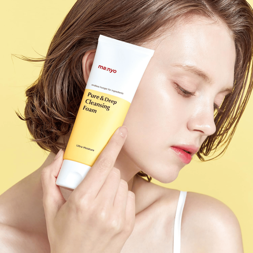 Woman with healthy, hydrated skin holding Ma:nyo Pure & Deep Cleansing Foam – gentle facial cleanser that provides radiance and balance with natural ingredients.