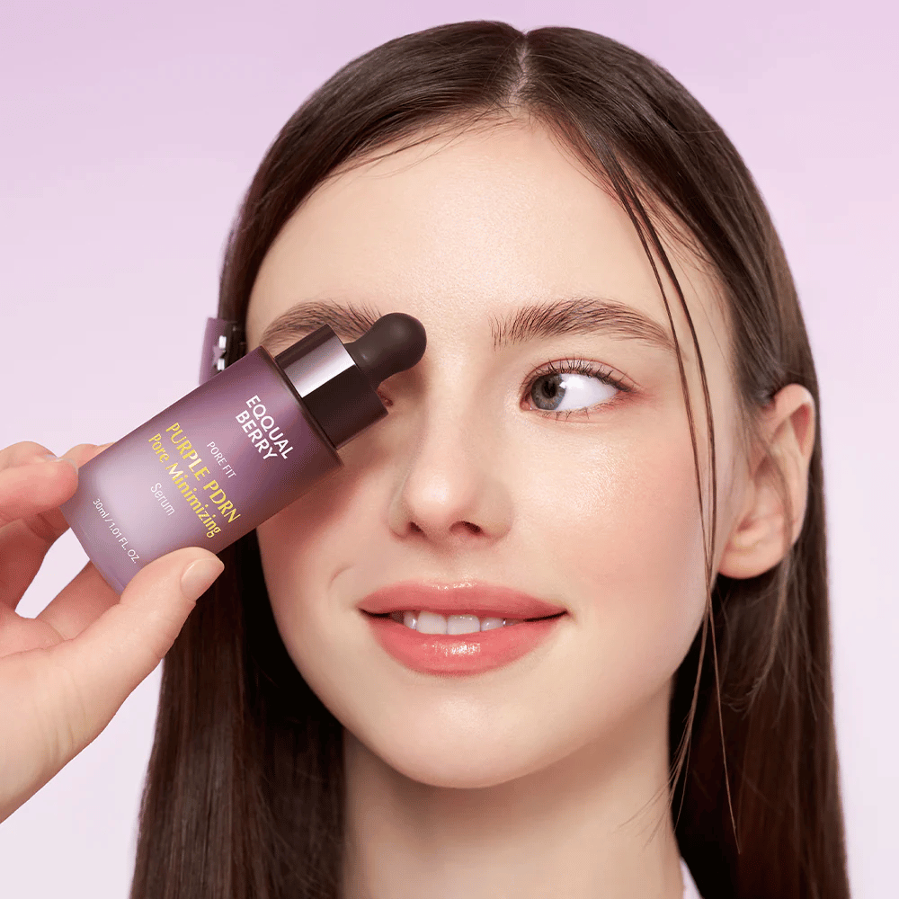 Young woman with smooth skin holds a bottle of Equal Berry Purple PDRN Pore Minimizing Serum against her forehead, against a light purple background.