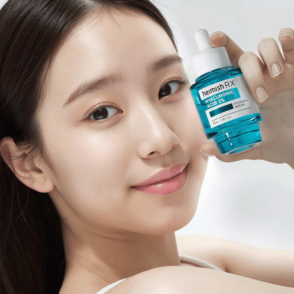 Smiling woman with radiant skin holding a bottle of Heimish RX Hyaluronic Acid 2% Hydrating Serum, highlighting its hydrating properties.