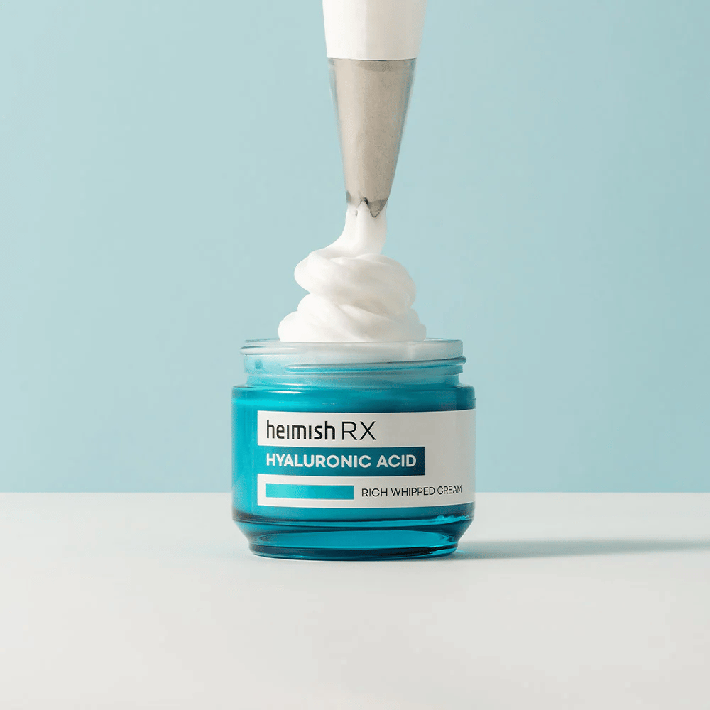 Heimish RX Hyaluronic Acid Rich Whipped Cream in a blue glass jar, where a piping bag applies the fluffy cream. A moisturizing face cream with hyaluronic acid for intense hydration and soft, plump skin.
