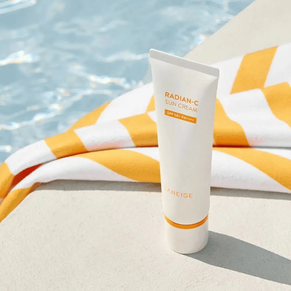 LANEIGE Radian-C Sun Cream står vid en poolkant med en gul- och vitrandig handduk i bakgrunden.