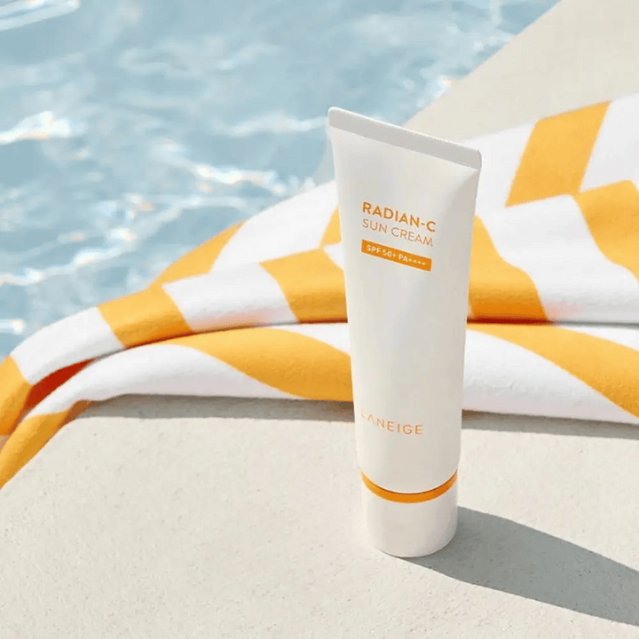 LANEIGE Radian-C Sun Cream står vid en poolkant med en gul- och vitrandig handduk i bakgrunden.