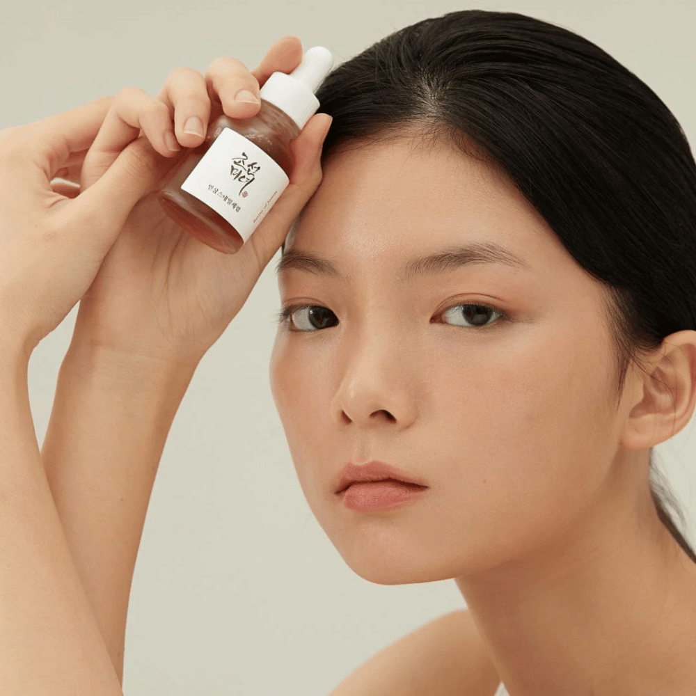 Modell håller Beauty of Joseon Revive Serum vid kinden – näringsrikt serum med ginseng och snigelslem.