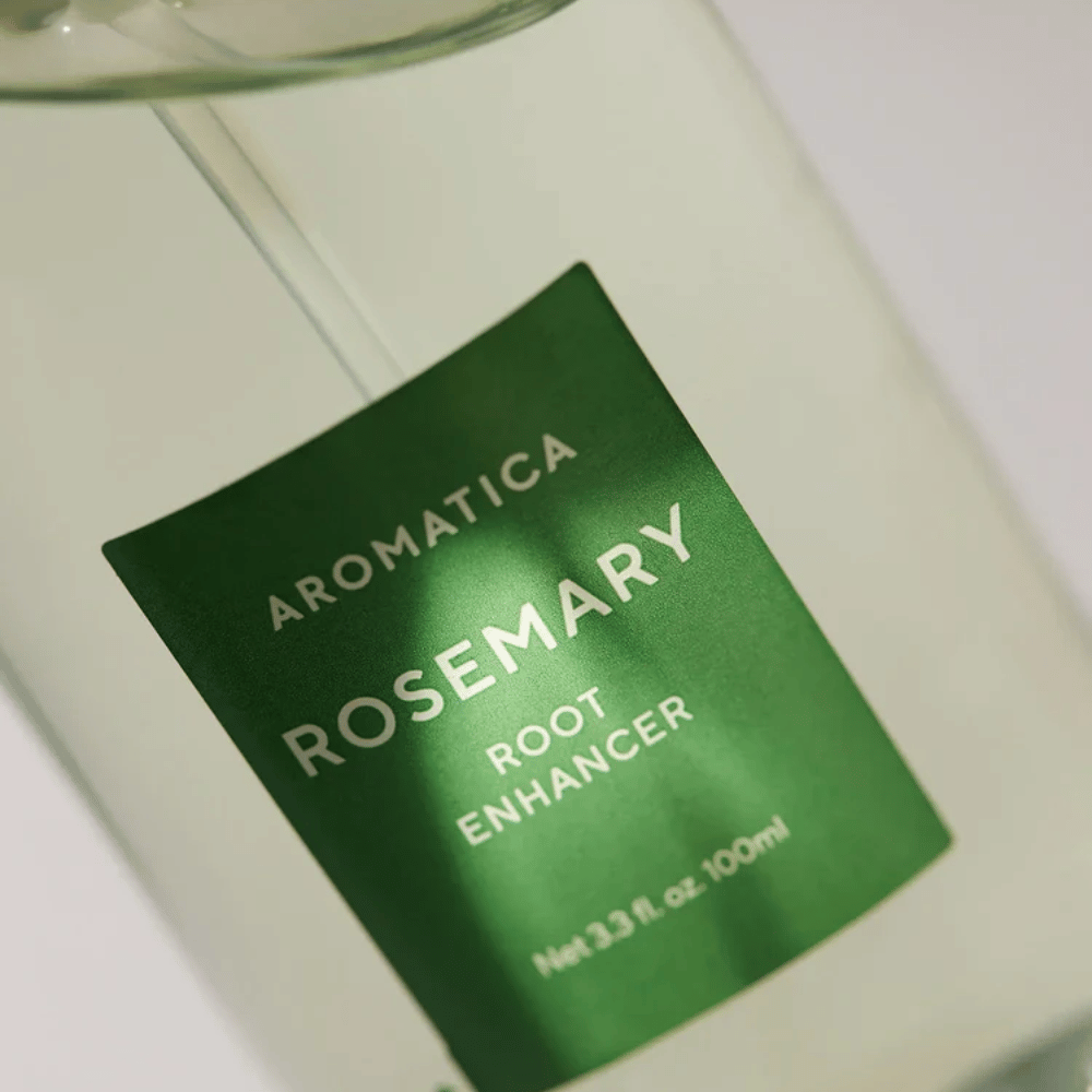 Close-up of the label on AROMATICA Rosemary Root Enhancer. The green label and the transparent bottle highlight the product's clean and minimalist appearance.