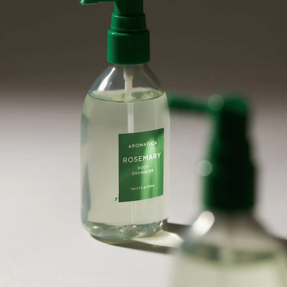 Close-up of AROMATICA Rosemary Root Enhancer with a green applicator nozzle. The image focuses on the bottle's design and the precise application directly onto the scalp.