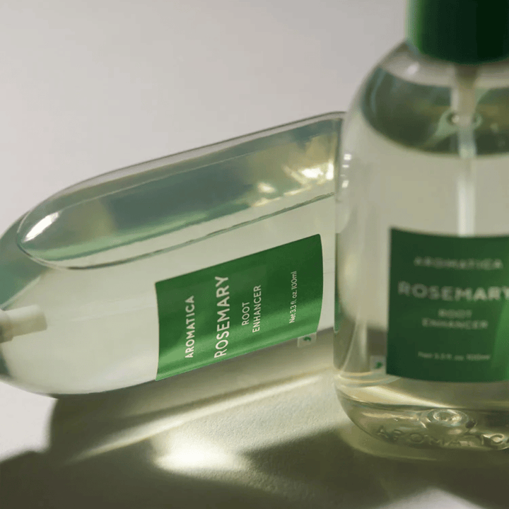 Two AROMATICA Rosemary Root Enhancer bottles with a transparent protective cap and green label. Close-up highlighting the product's premium design and natural hair care concept.