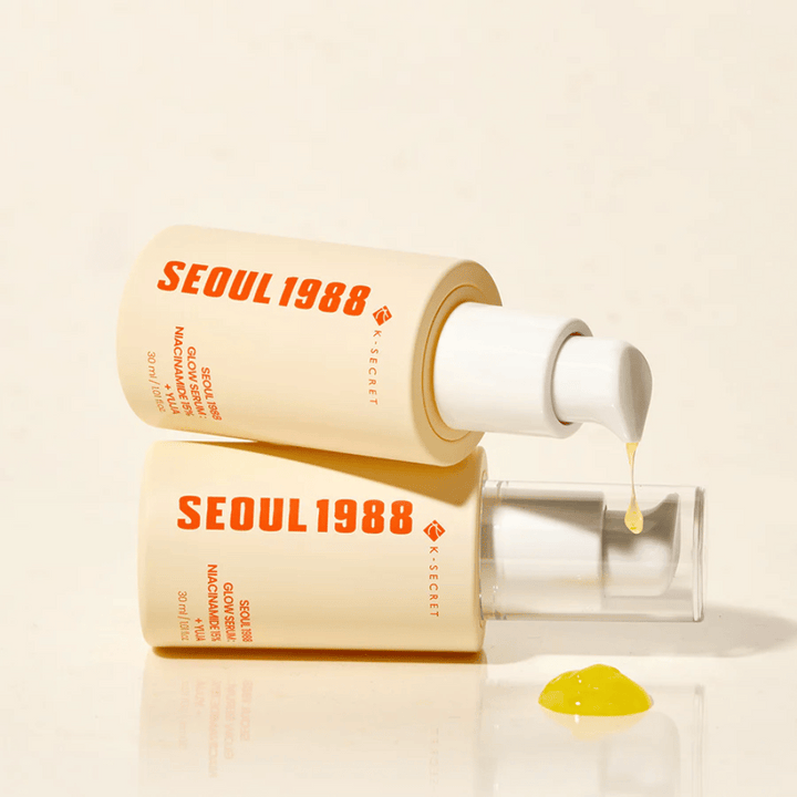 Två flaskor Seoul 1988 Glow Serum liggande och stående, med gult serum droppande ur pumpen.