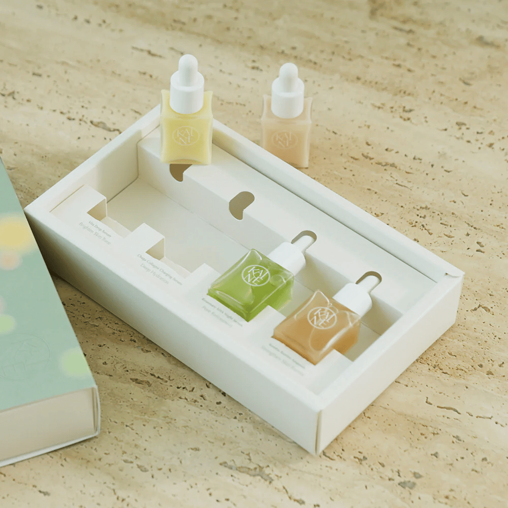 Four colorful serum bottles from KAINE Serum Discovery Kit with pipette caps, designed to meet various skin needs in a minimalist and sleek packaging.