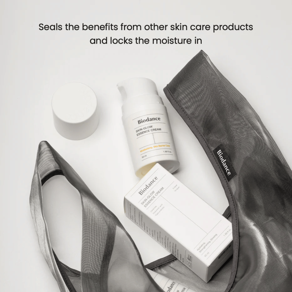 Biodance Skin-Glow Essence Cream standing in focus along with the product packaging and a black transparent toiletry bag, with text above emphasizing the cream's ability to lock in moisture and enhance the effect of other skincare products.