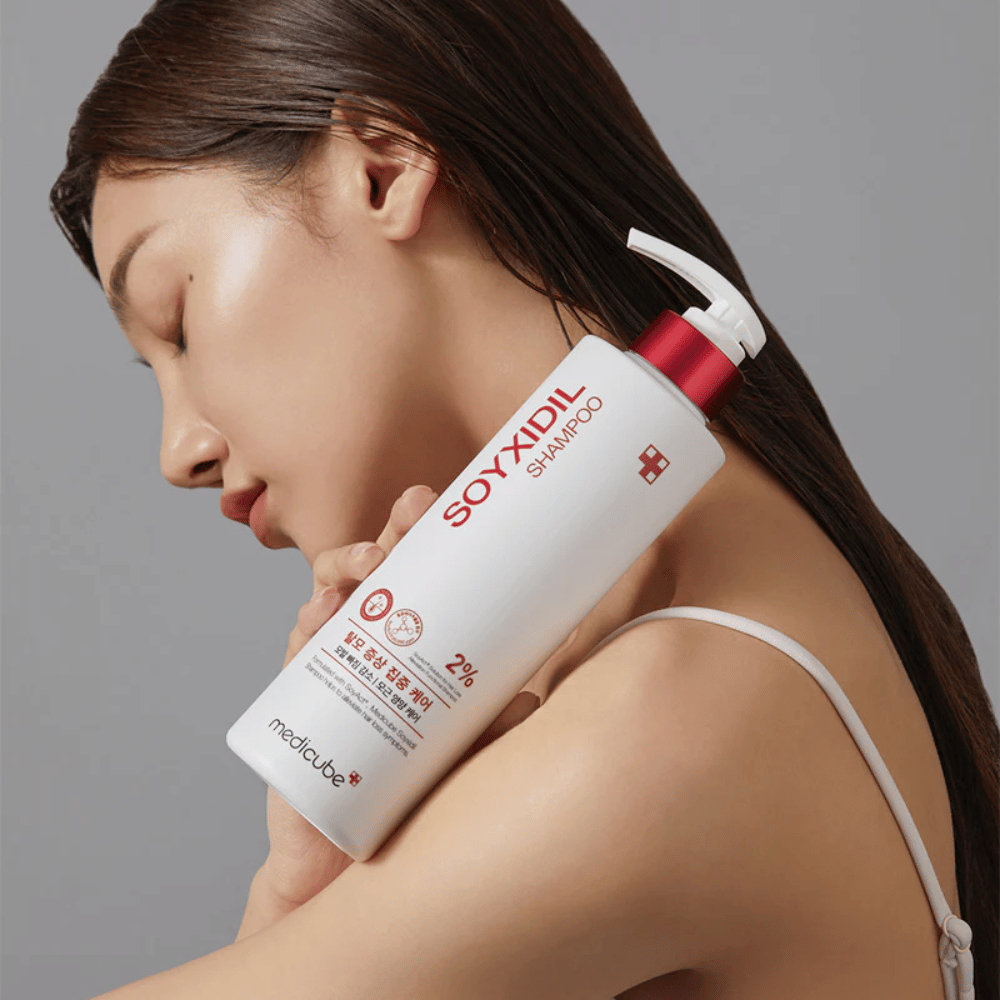 Woman with long hair leans her head against a bottle of Medicube Soyxidil Shampoo, which strengthens the scalp and prevents hair loss.