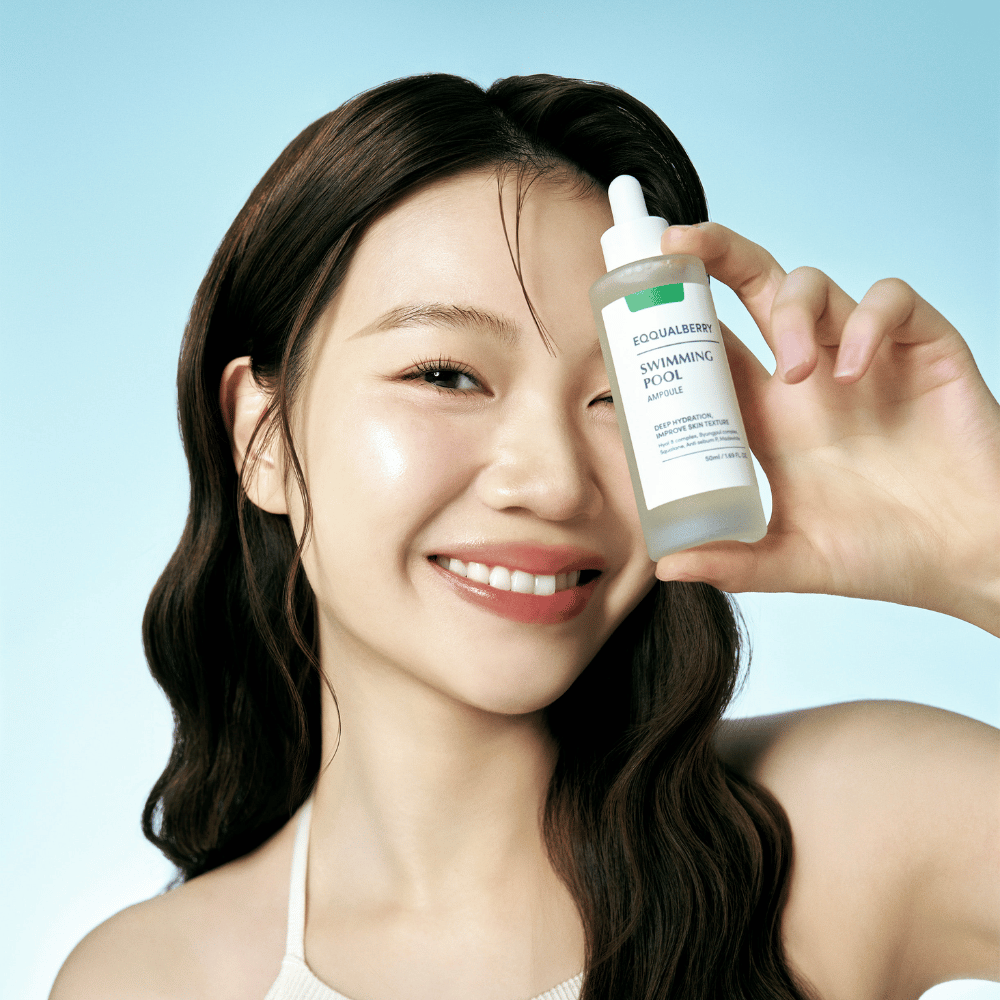 A smiling woman holds up Eqqualberry Swimming Pool Ampoule, a skincare product for intensive hydration, in front of a light blue background.