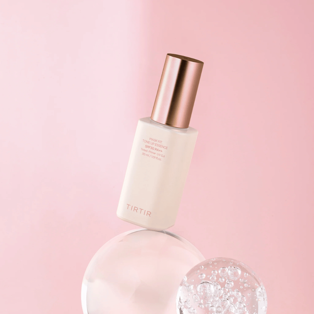 The image shows a bottle of "TIRTIR MASK FIT TONE UP ESSENCE" with SPF30 PA++ against a pink background, giving a sense of softness and femininity.