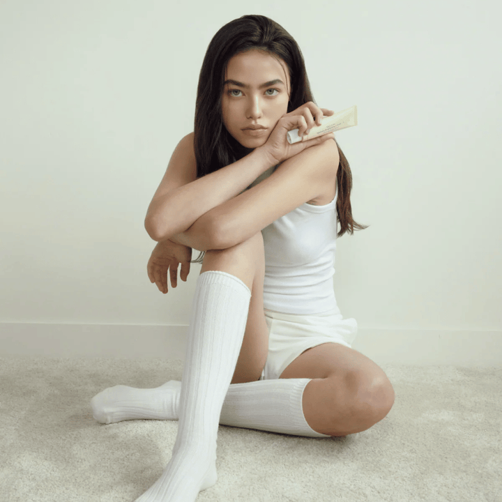 Lifestyle image with a model holding the product in a bright and minimalist environment. The image conveys a clean, natural, and calm skincare feel connected to glow and brightening effect.