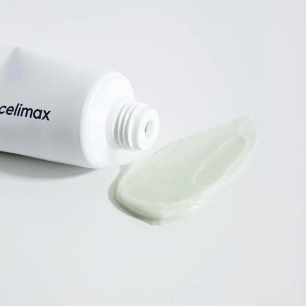 Celimax Noni Energy Repair Cream in a white tube with a small amount of light green cream spread next to the tube on a white surface. The cream is for nourishing and repairing the skin.