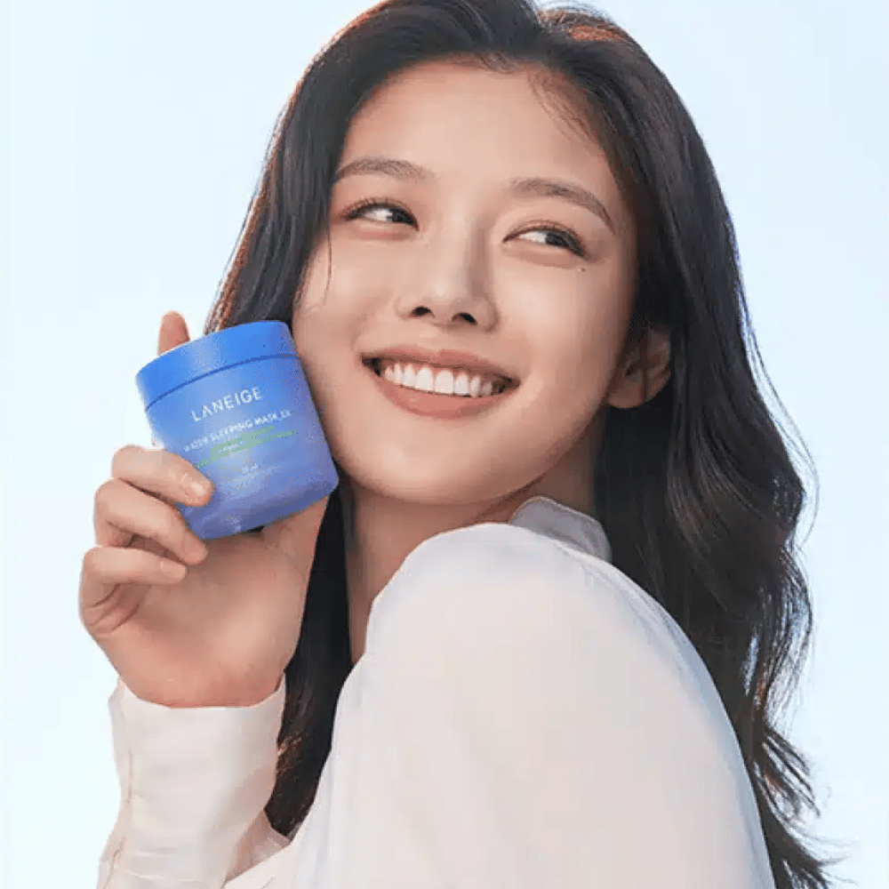 Smiling woman holds up a blue jar of LANEIGE Water Sleeping Mask in front of a light blue background.