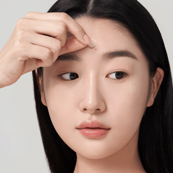 Person applying Purito Wonder Releaf Centella Spot Patch on a pimple on the forehead, a discreet acne patch that protects, soothes, and supports skin healing.