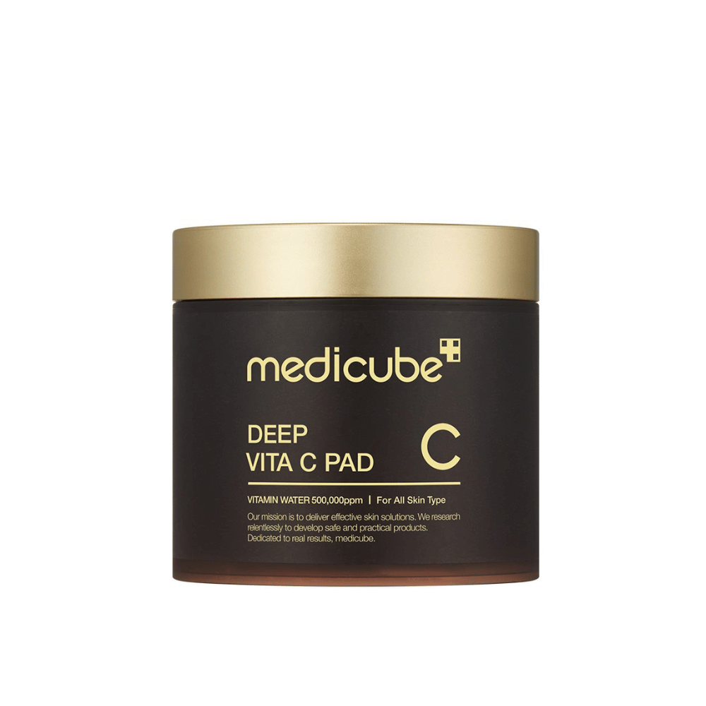 A jar from medicube, labeled "Deep Vita C Pad", with a gold lid and dark body. Text on the jar indicates vitamin C and suitability for all skin types. The background is neutral.